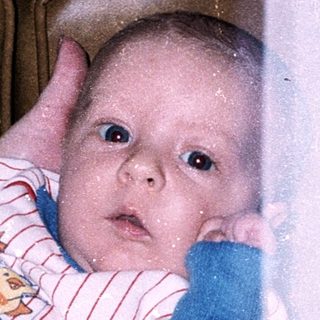 Baby in bathtub with teddy and hands visible.