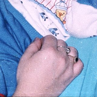 Baby in bathtub with teddy and hands visible.