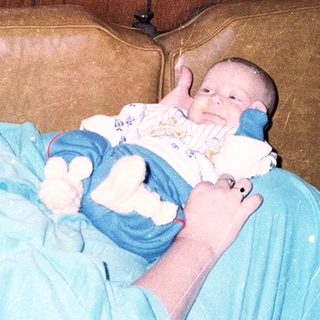 A woman in medical scrubs holds a newborn baby.