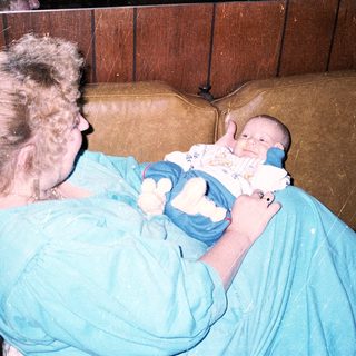 A woman in medical scrubs holds a newborn baby.