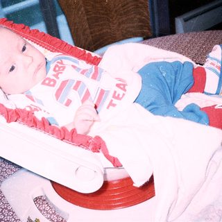 Baby wearing "Baby Team" onesie in car seat.