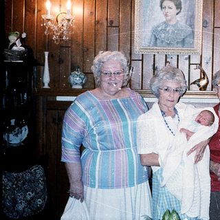Family gathering holding newborn baby indoors.