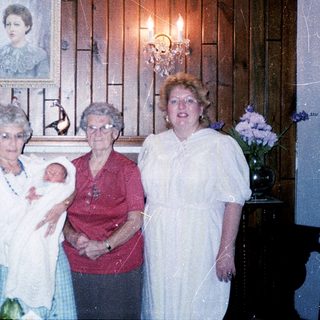 Four women posing with a baby indoors.