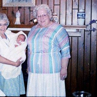 Two elderly women holding a newborn baby indoors.