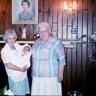 Two elderly women holding a newborn baby indoors.