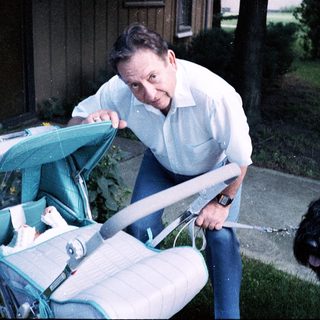 Man pushing stroller with baby inside, dog nearby.
