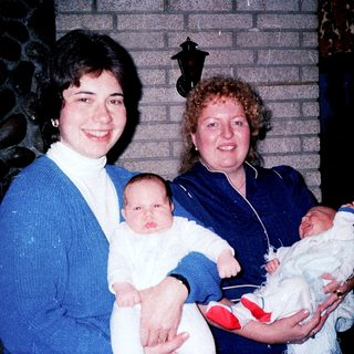 Two women holding newborn babies indoors.