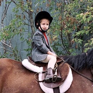 Child riding horse in outdoor arena.