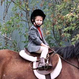 Child riding horse in outdoor riding arena.