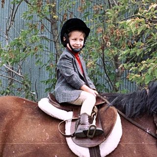 Child riding a horse in outdoor arena.