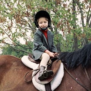 Child riding a horse in an outdoor paddock.