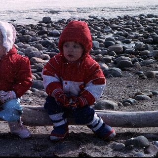Two children playing on a rocky beach in winter.