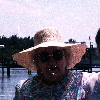 Two women smiling by water, wearing summer attire.
