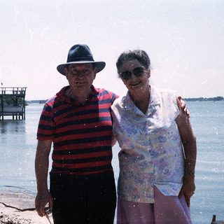Two elderly people posing by a waterfront pier.