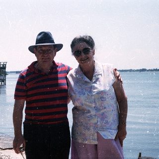 Two elderly people posing by a waterfront pier.
