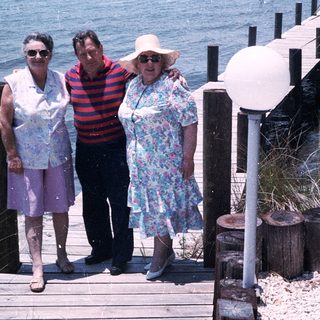 Three people posing on a seaside boardwalk.