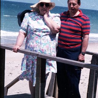 Two elderly people standing on beach stairs by ocean.