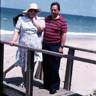 Two elderly people standing on beach stairs by ocean.