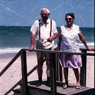 Two elderly people standing on beach stairs by ocean.