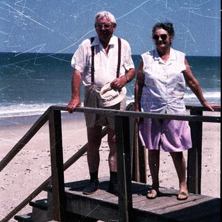 Two elderly people standing on beach stairs by ocean.