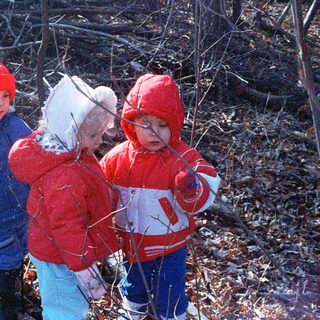 Three children in winter clothing playing outdoors in snow.
