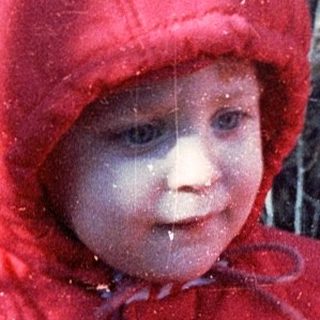 Young child wearing red and white winter jacket outdoors.