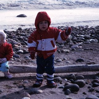 Two children playing on rocky beach near ocean.