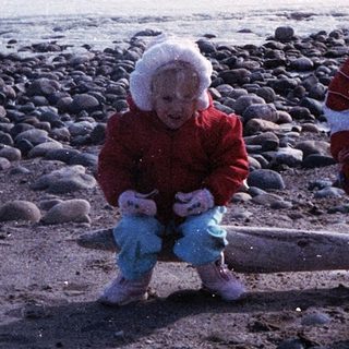 Two children playing on rocky beach near ocean.