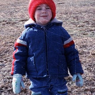 Young child wearing winter gear playing outdoors.