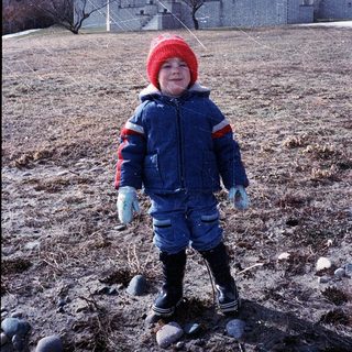 Young child wearing winter gear playing outdoors.