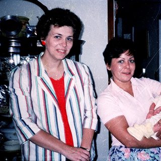 Two women posing with a newborn baby indoors.