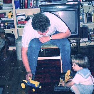 Man helping child play with toy car.