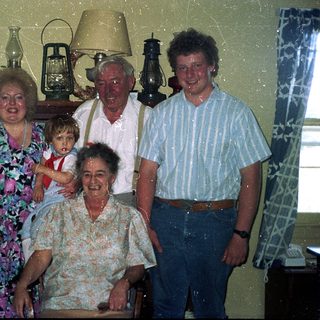 Family group photo with elderly and young relatives indoors.