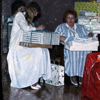 Three women wrapping gifts in festive setting.
