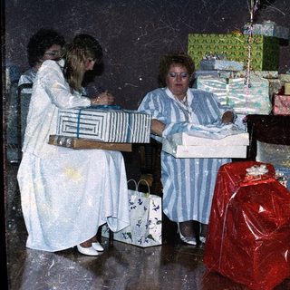 Three women wrapping gifts in festive setting.
