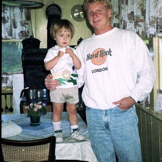 Man and young child posing indoors near kitchen.