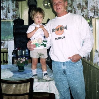 Man and young child posing indoors near kitchen.