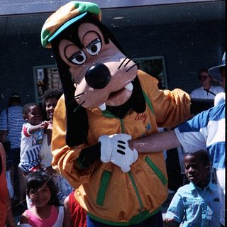 Costumed Goofy interacting with crowd outdoors.