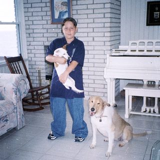 Person holds small dog indoors with larger dog sitting nearby.