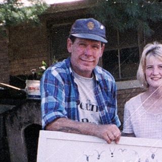 Three people holding a quilt with various appliquéd designs.