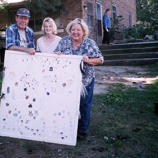 Three people holding a quilt with various appliquéd designs.