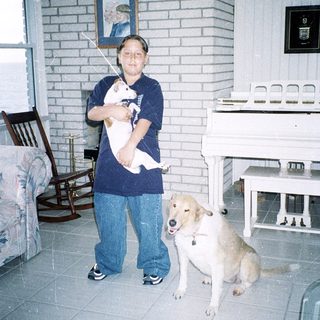 Person holding a white kitten indoors with a dog.