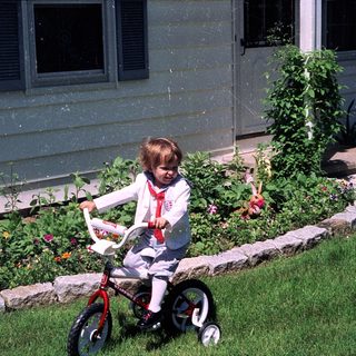 Young child riding small bicycle near garden.