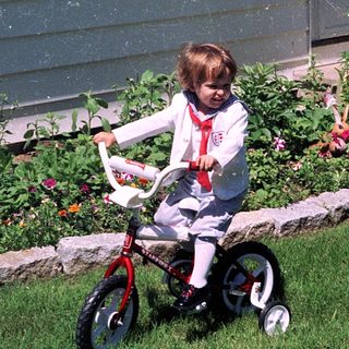 Young child riding small bicycle near garden.