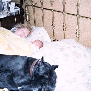 A baby and a black cat peacefully sleeping together in bed.