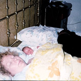 Newborn sleeping beside mother in hospital bed.