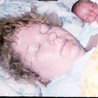 Newborn sleeping beside mother in hospital bed.
