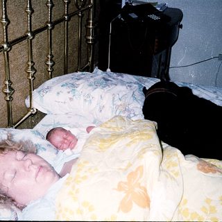 Newborn sleeping beside mother in hospital bed.