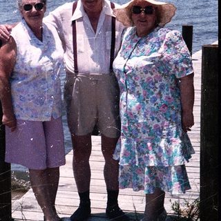 Three elderly people posing together by a waterfront dock.