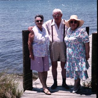 Three elderly people posing together by a waterfront dock.